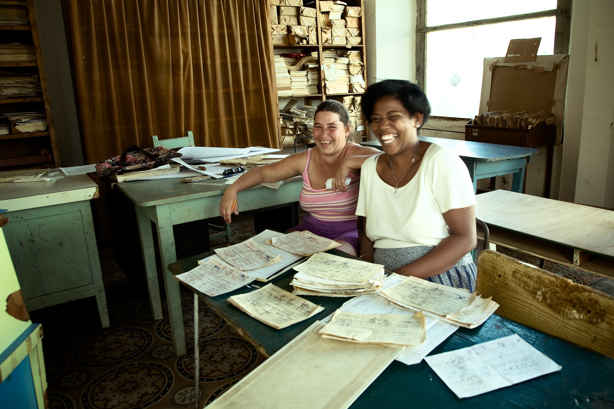 Deux femmes souriantes à un bureau couvert de papiers, Caibarién, Villa Clara, Cuba