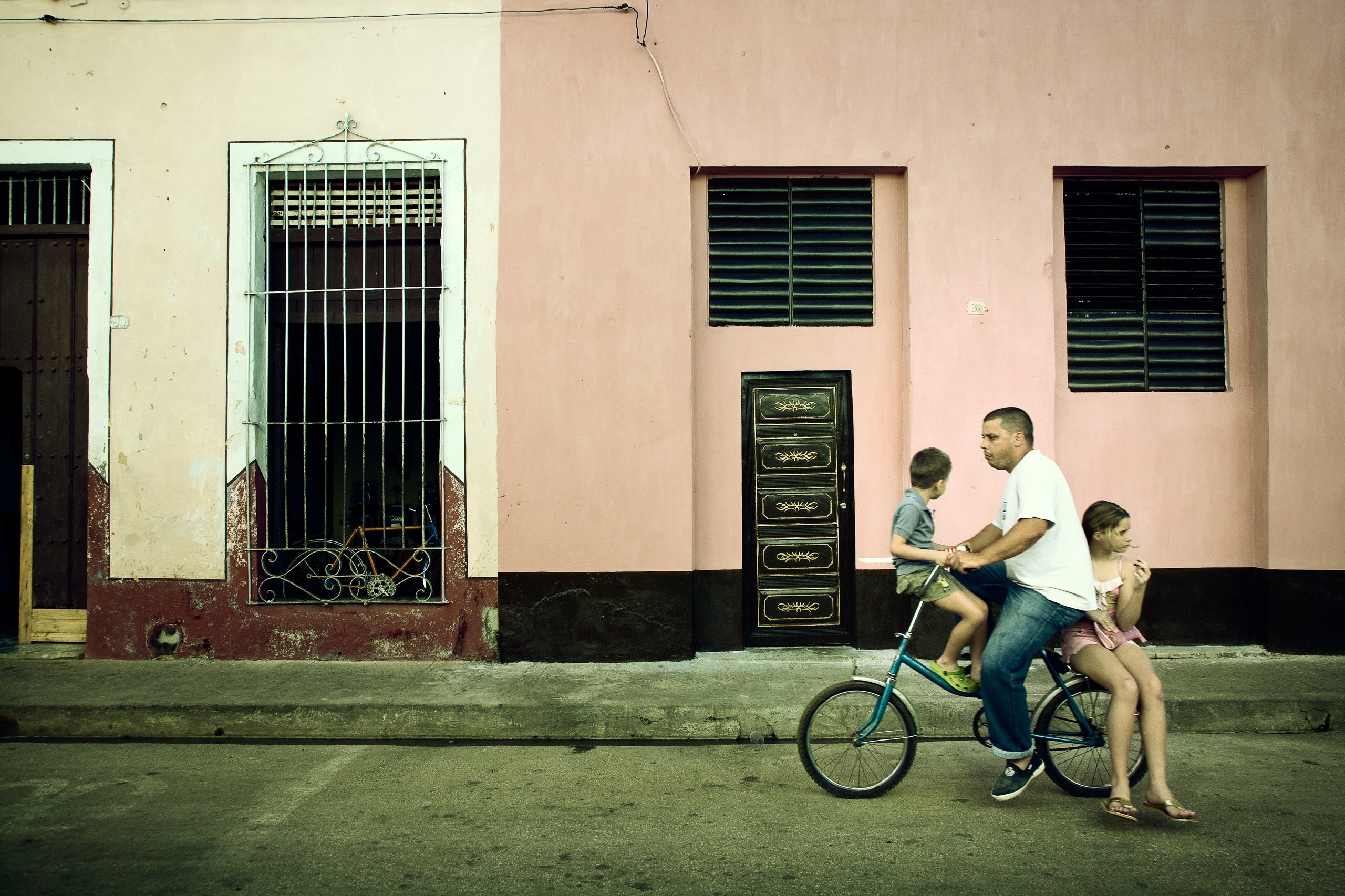 Un homme et deux enfants à vélo devant une façade rose, Caibarién, Villa Clara, Cuba